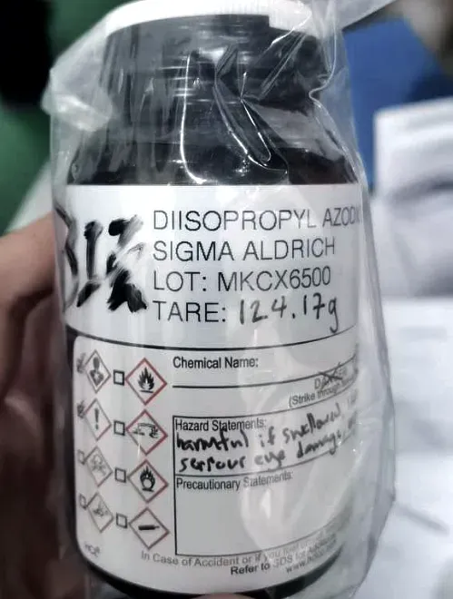 A research reagent bottle in a sealed bag, carrying a GHS hazard label with its statements written in by hand